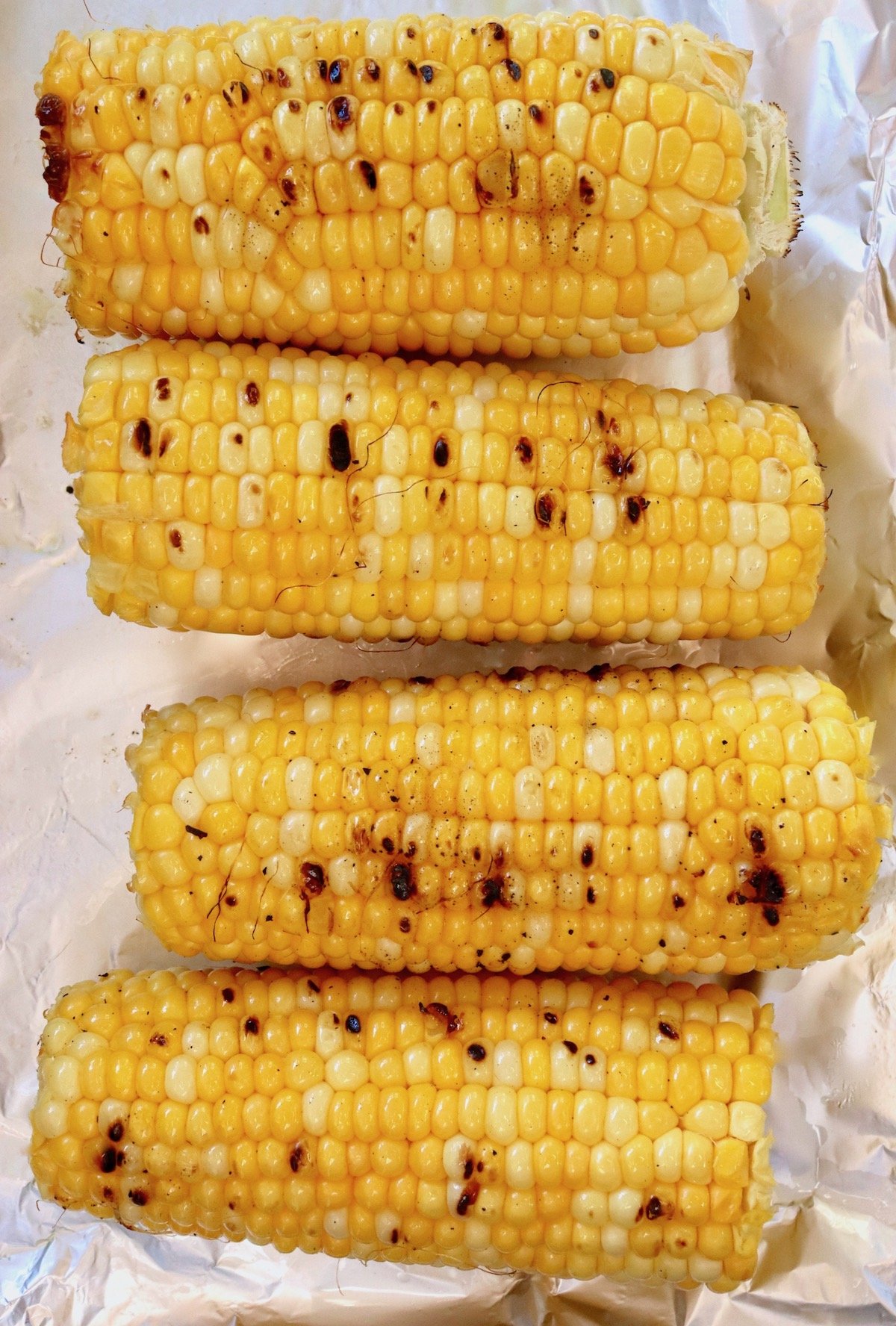 Four ears of charred corn on foil-lined baking sheet.