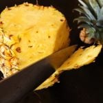 whole pieapple with skin being removed with Chef's knife