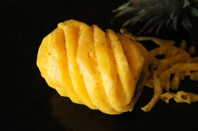 peeled pineapple on its side with diagonal cuts in it