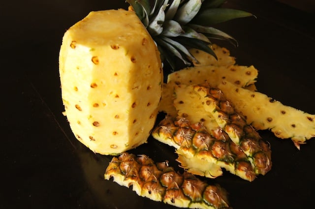 peeled pineapple standing with peels and stem next to it