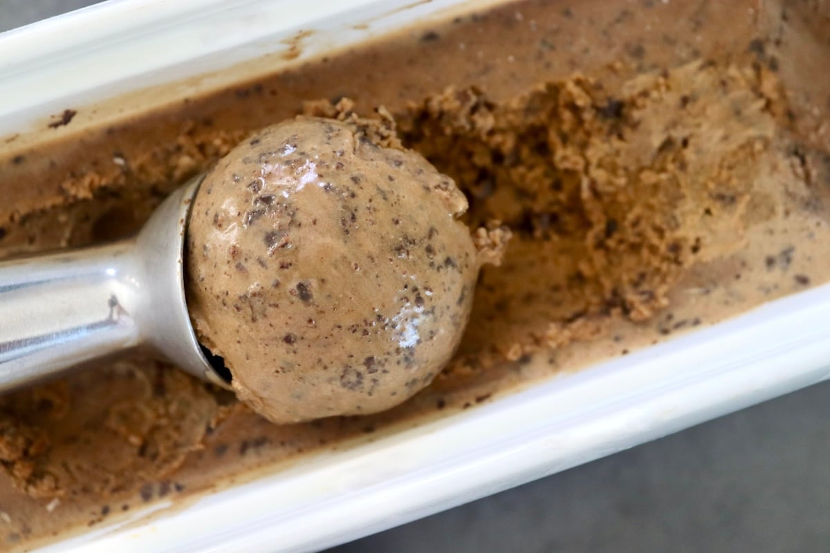 Espresso chip gelato in an ice cream container with a scoop scooping a perfect scoop on top.