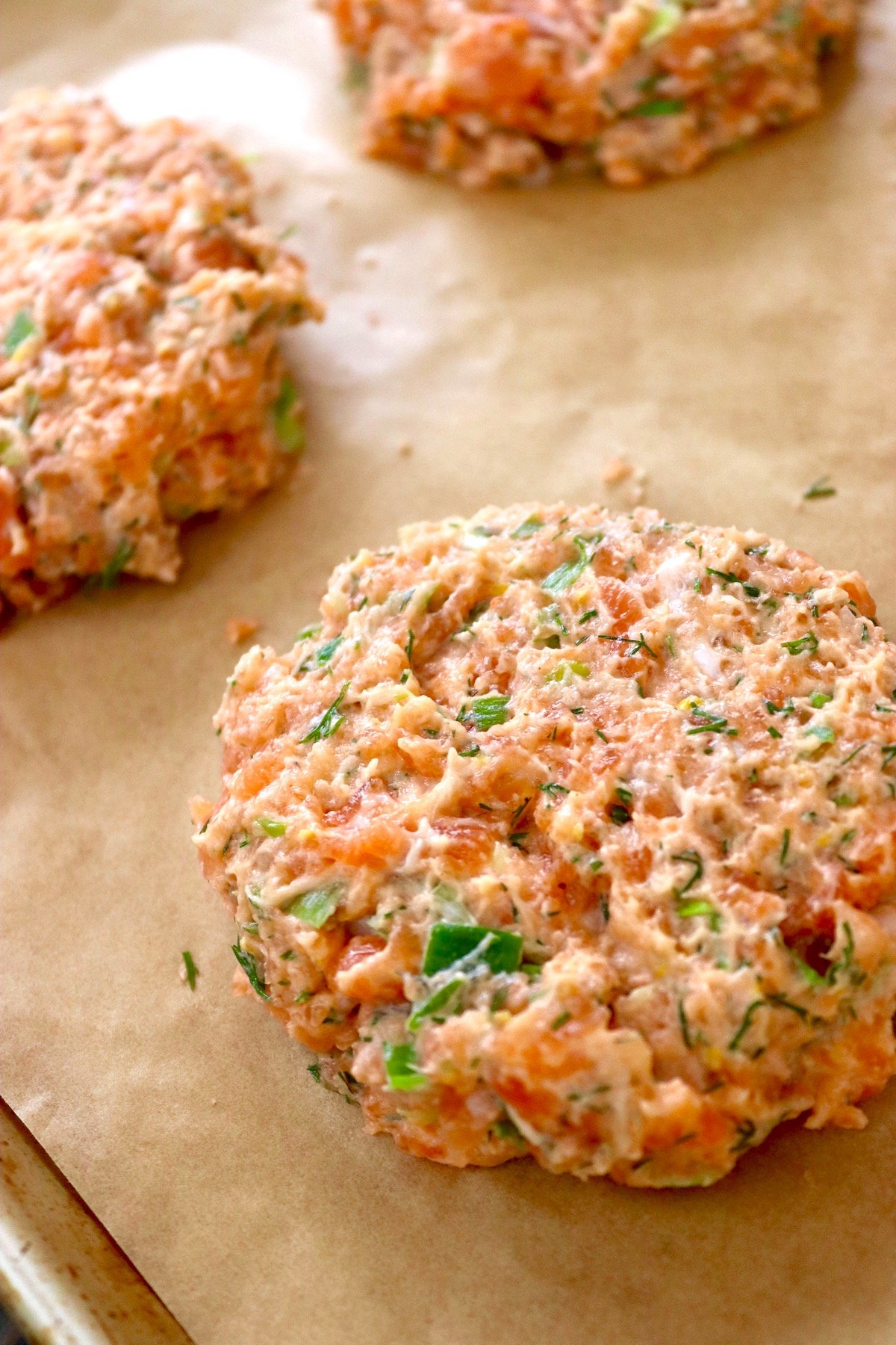 Raw salmon patties on parchment paper on baking sheet.