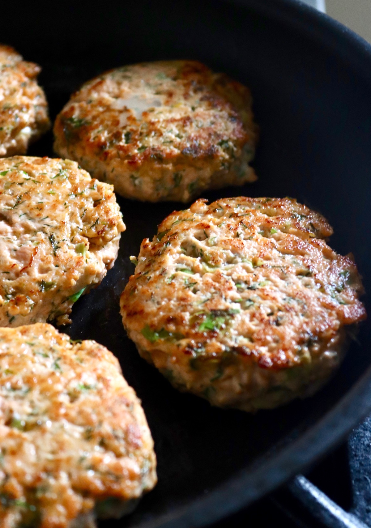 Golden brown salmon patties in dark saute pan.