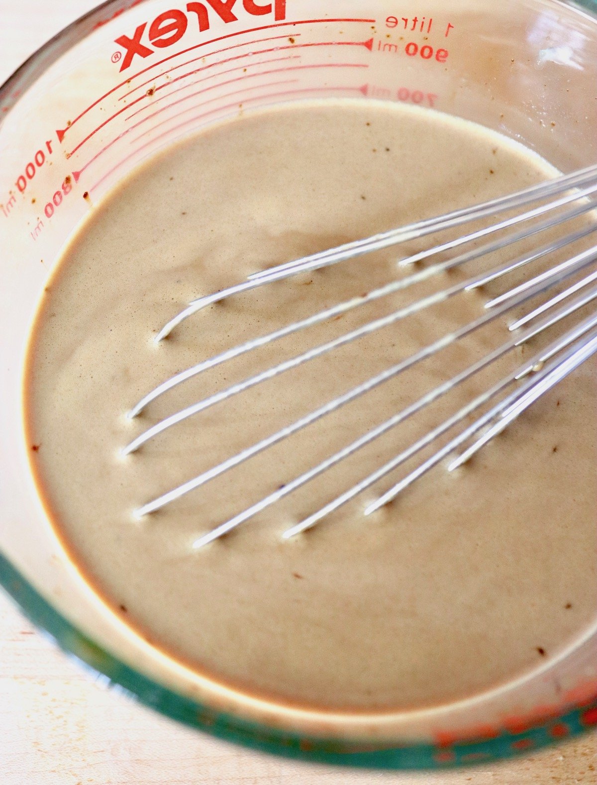 Creamy coffee mixture in a pyrex measuring glass with a whisk.