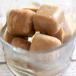 Clear drinking glass with several creamy coffee ice cubes in it.