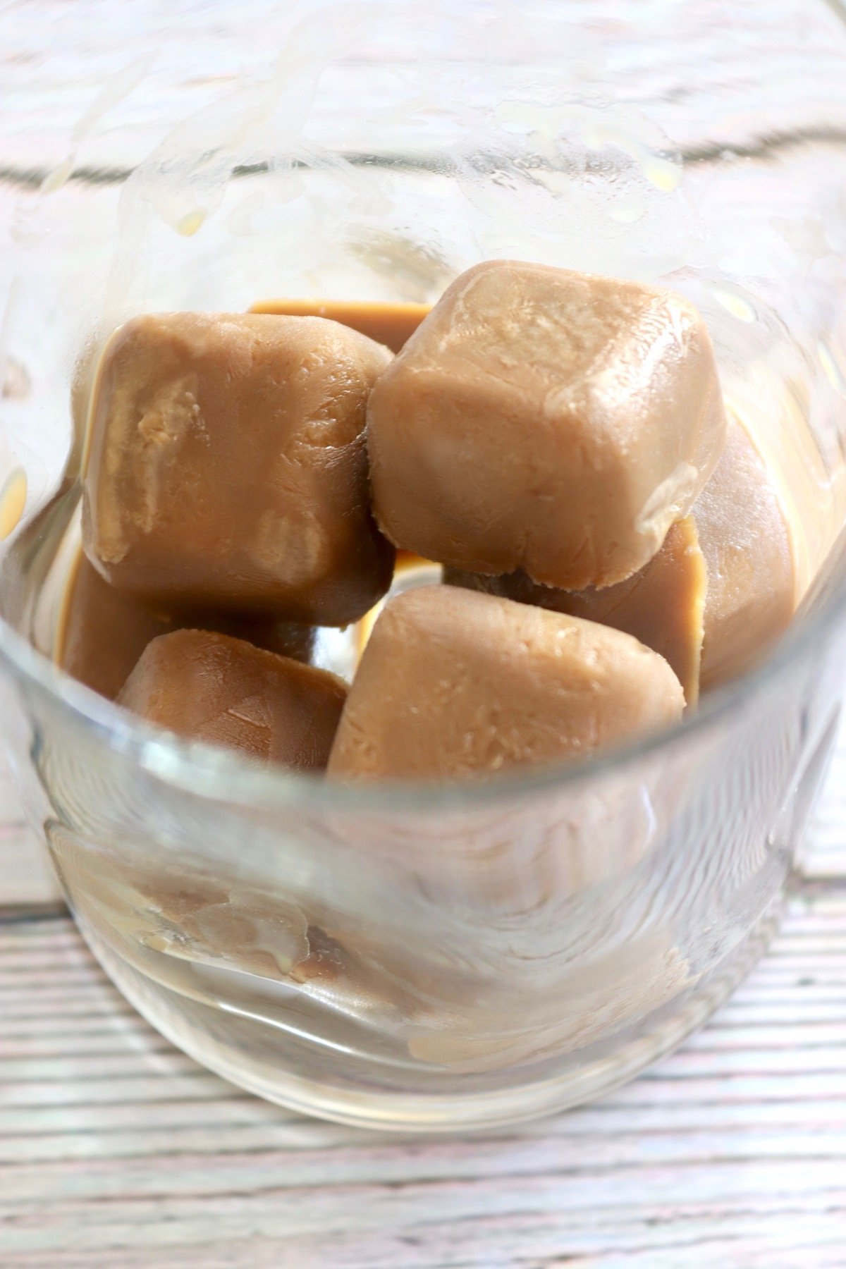 Clear drinking glass with several creamy coffee ice cubes in it.