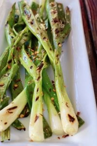Several grilled scallions on a white plate.