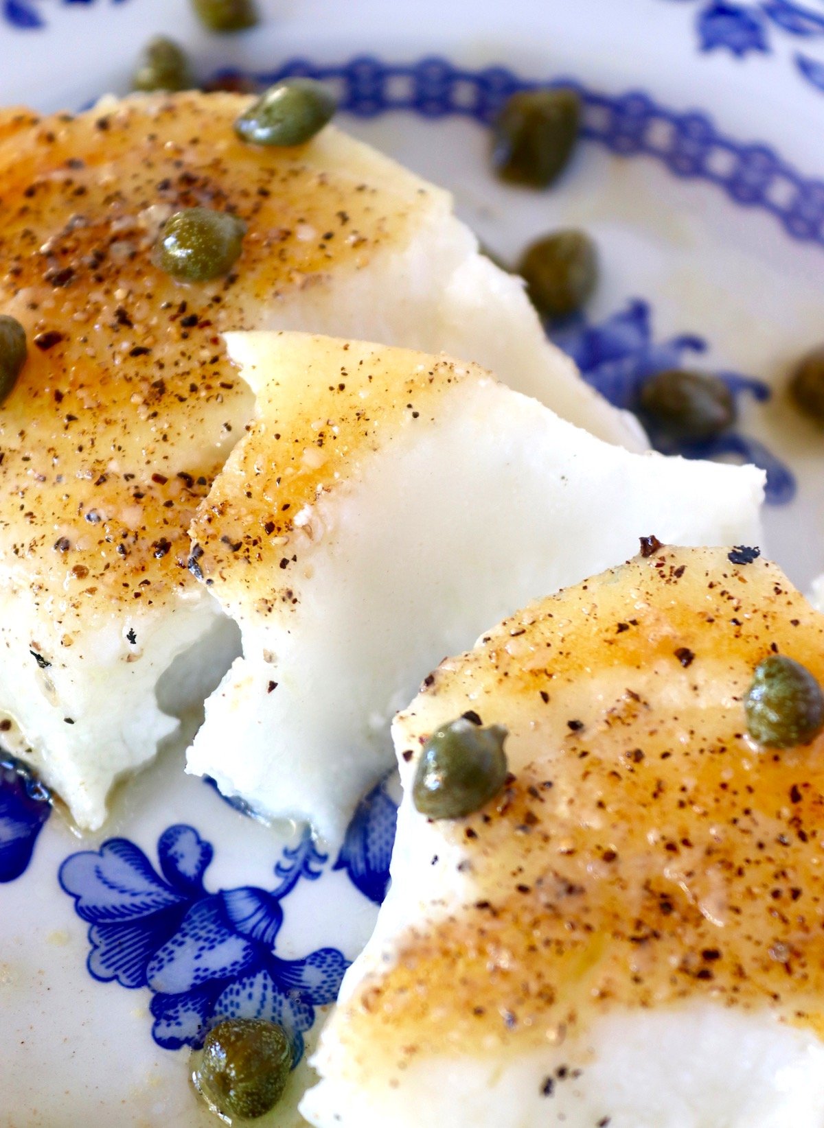 Seared and flaked Chilean Sea Bass (Patagonian Toothfish) on a blue and white plate with lemon-caper sauce.