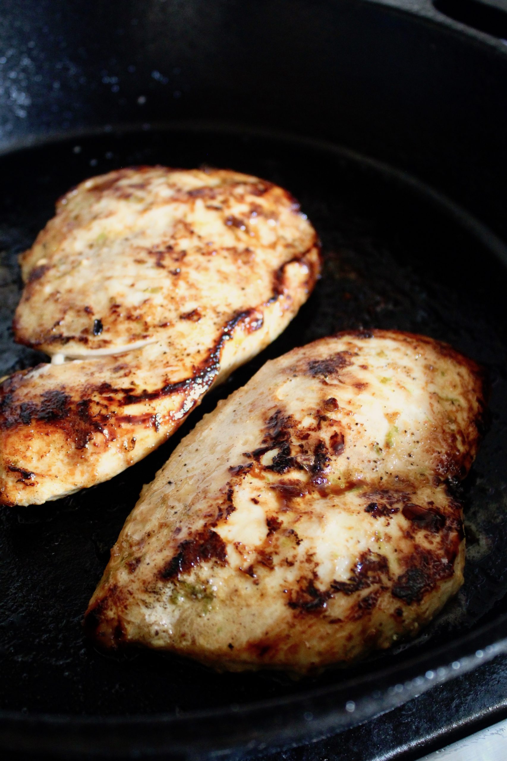 two sautéed chicken breasts in cast iron skillet