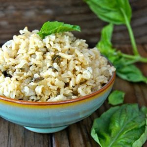 green-blue bowl with brown rim filled with basil rice, surrounded with fresh basil leaves