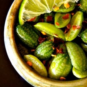 close up of cucamelons in a beige bowl with chili flakes and lime