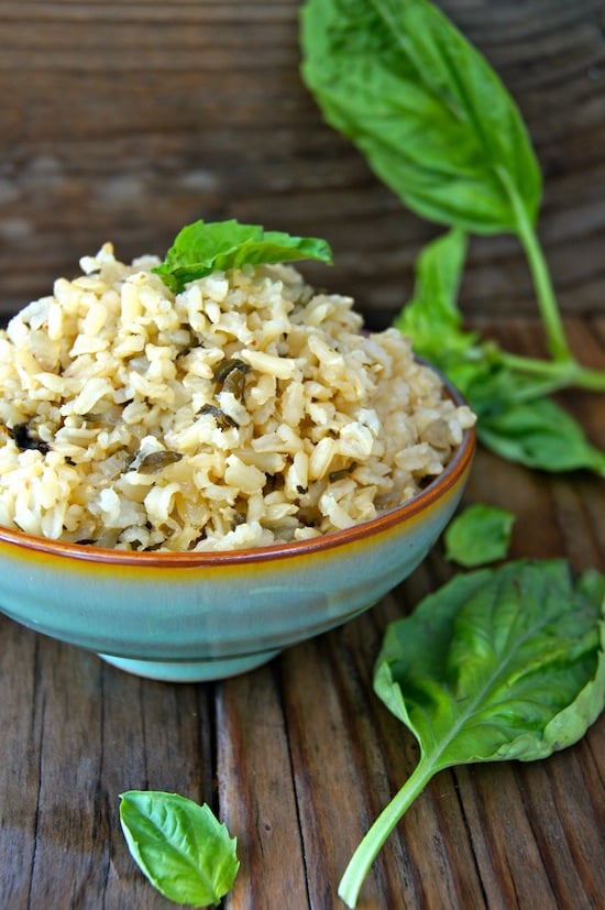 Roasted Garlic-Basil Brown Rice in s mint green ceramic bowl surround by fresh basil leaves
