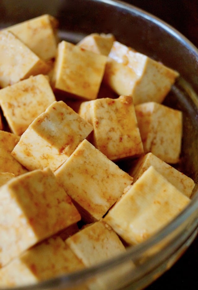 Tofu cubes in a Sesame Sriracha Honey marinade in a glass bowl.