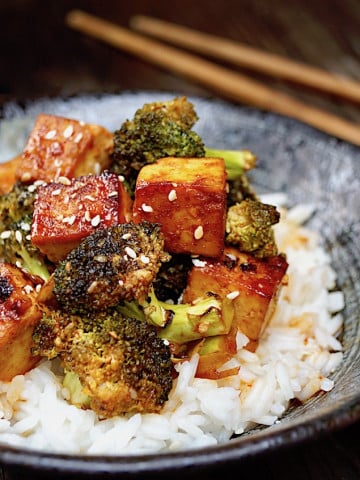 Sesame Sriracha Honey Tofu Broccoli in a black bowl with wooden chopsticks.