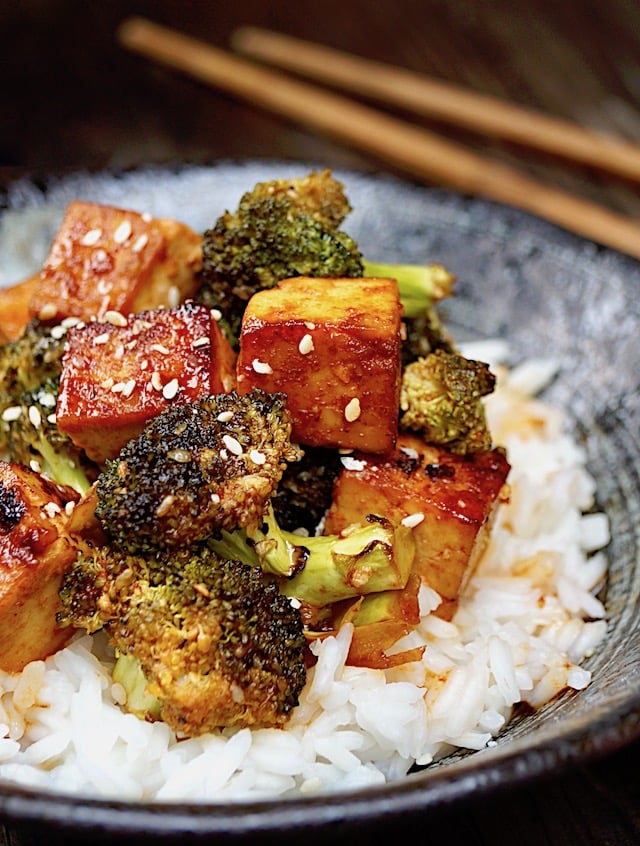  Sesame Sriracha Honey Tofu Broccoli in a black bowl with wooden chopsticks.