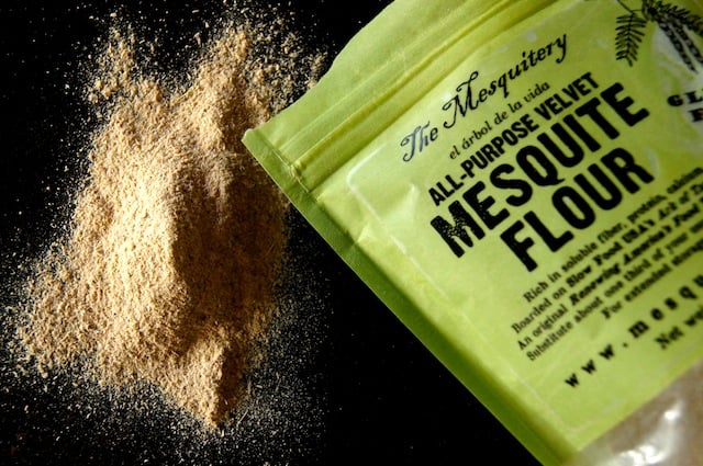 Bag of mesquite flour with some spilled out onto dark table.