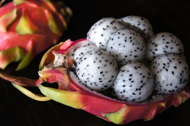 Magenta dragon fruit half full of balls of the white and black speckled flesh.