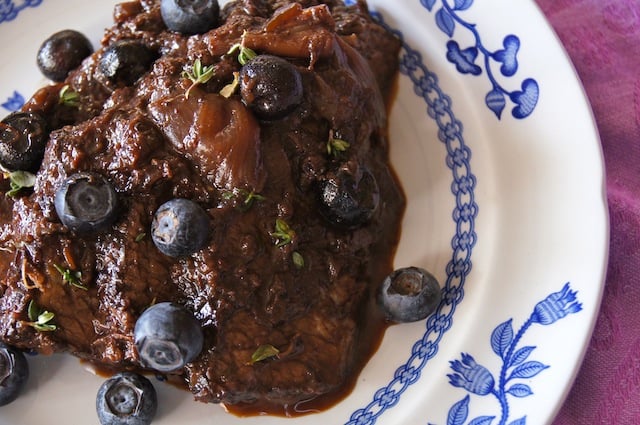 Blueberry Balsamic Braised Brisket on a white and blue plate with fresh blueberries