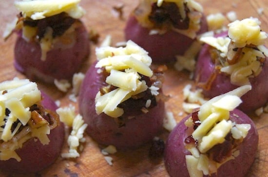 grated cheese on top of halved tiny red potatoes on cutting board