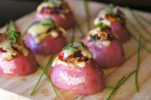 Six Mini Red Potato Appetizer with Cranberries on light cutting board with chives.