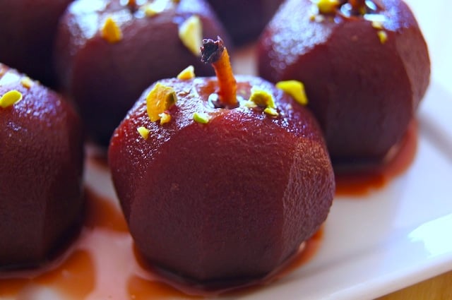 A few red wine poached tiny apples with pistachio pieces on them.