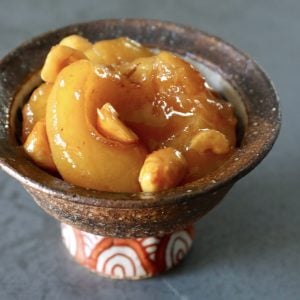 Small brown ceramic bowl with orange-patterned stem, filled with baked caramel apples and hazelnuts.