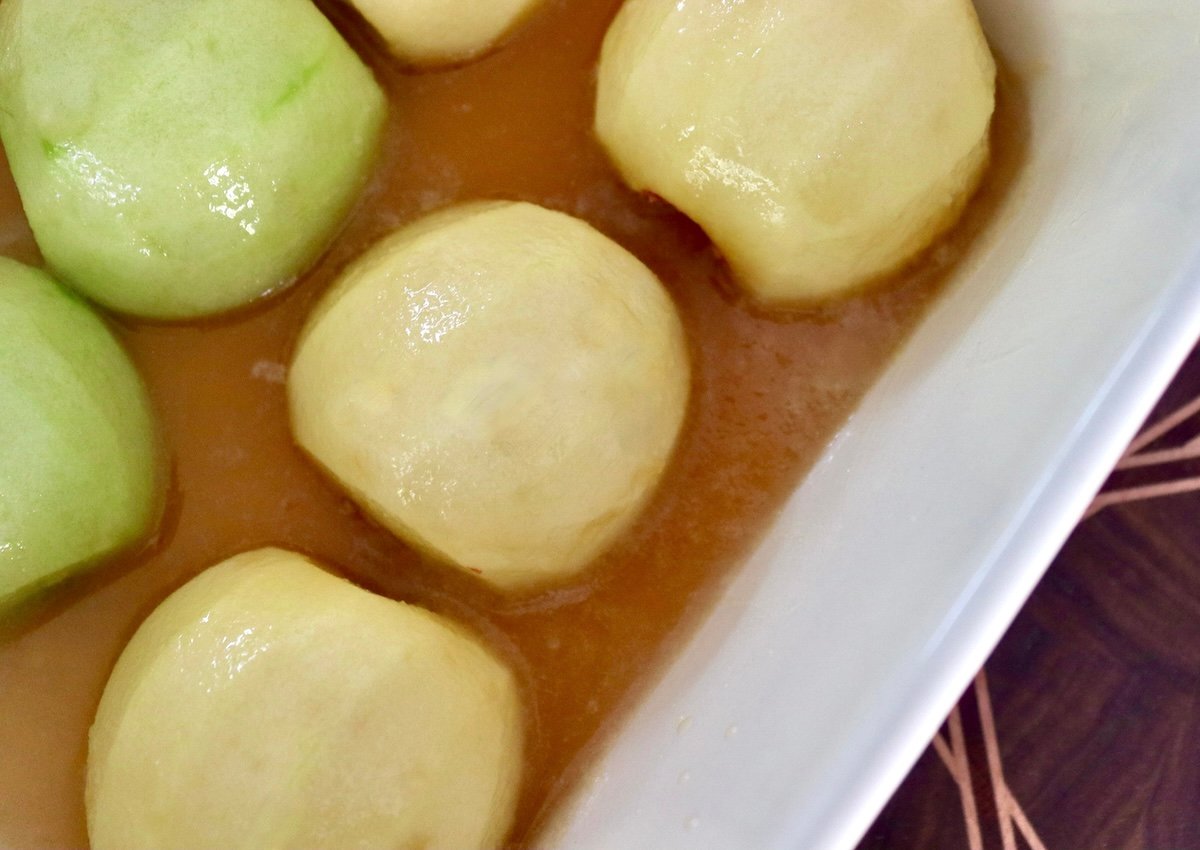 Peeled apple halves, round sides up, in a baking dish in syrup.