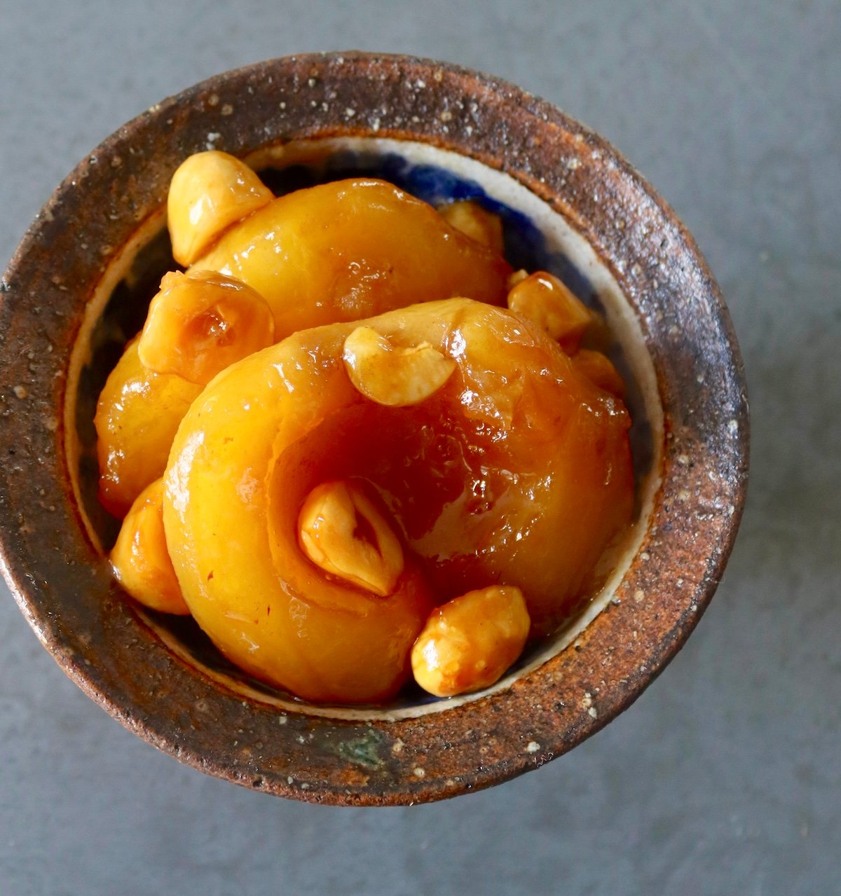 Close up, top view of baked apples with hazelnut syrup and chopped hazelnuts, in a small brown ceramic bowl.