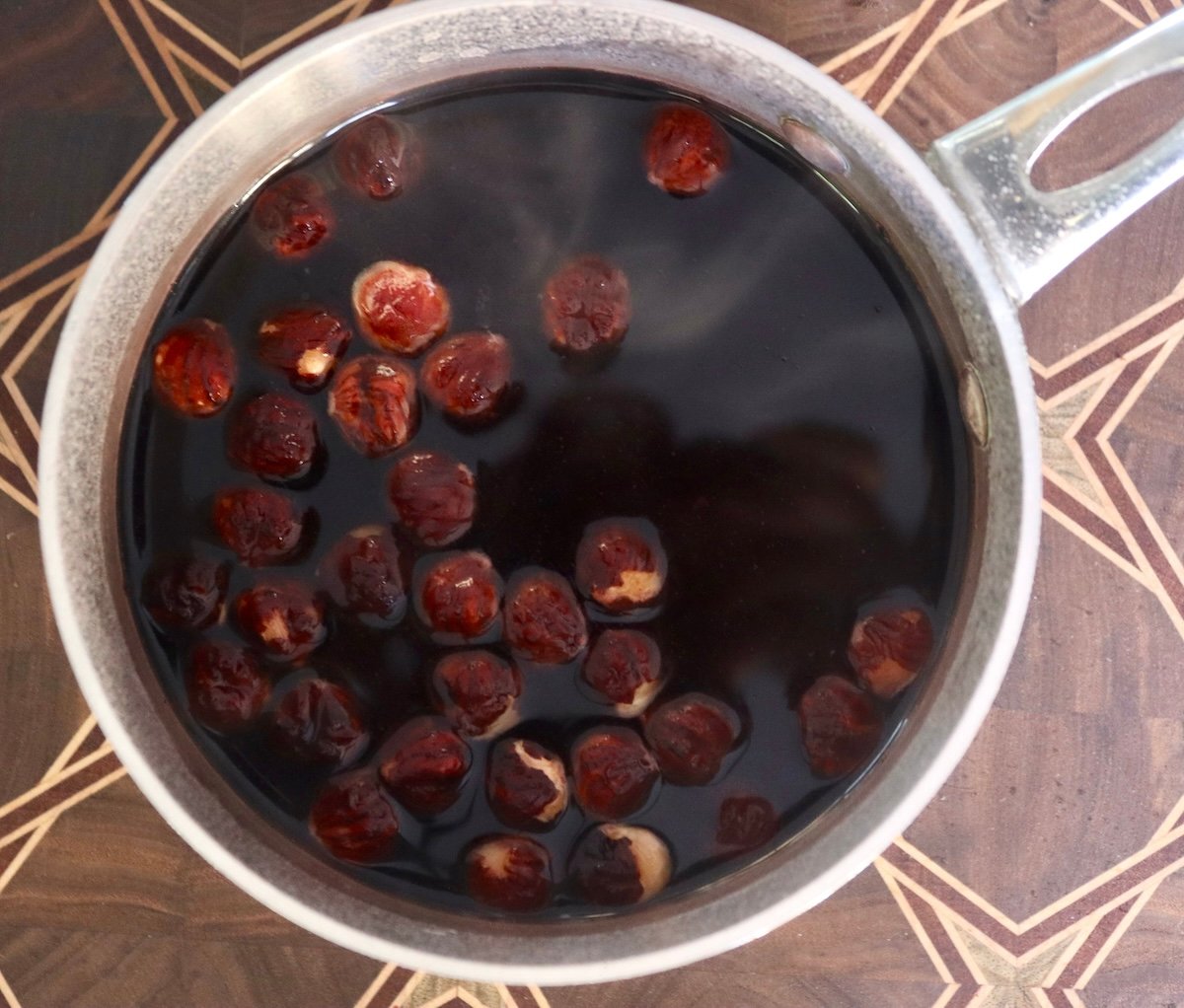 Hazelnuts with skin on dark brown water (from the skin) in a small pot with water.