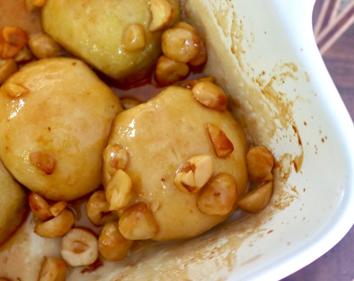 Peeled apple halves, round sides up, golden-baked in a baking dish with syrup and hazelnuts.