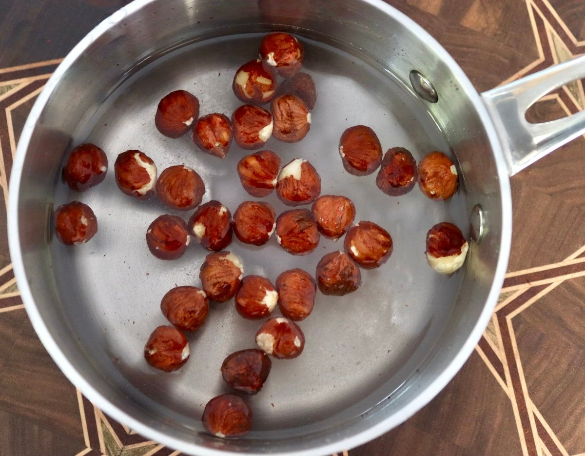 Hazelnuts with skin on in a small pot with water.