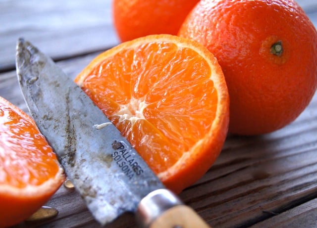 Tangerine being sliced in half with 2 whole tangerines in the background