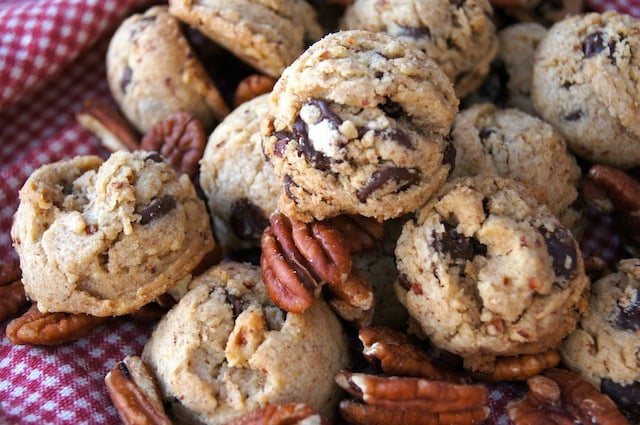 A pile of Pecan Praline Chocolate Chip Cookies on a red and white checked cloth.