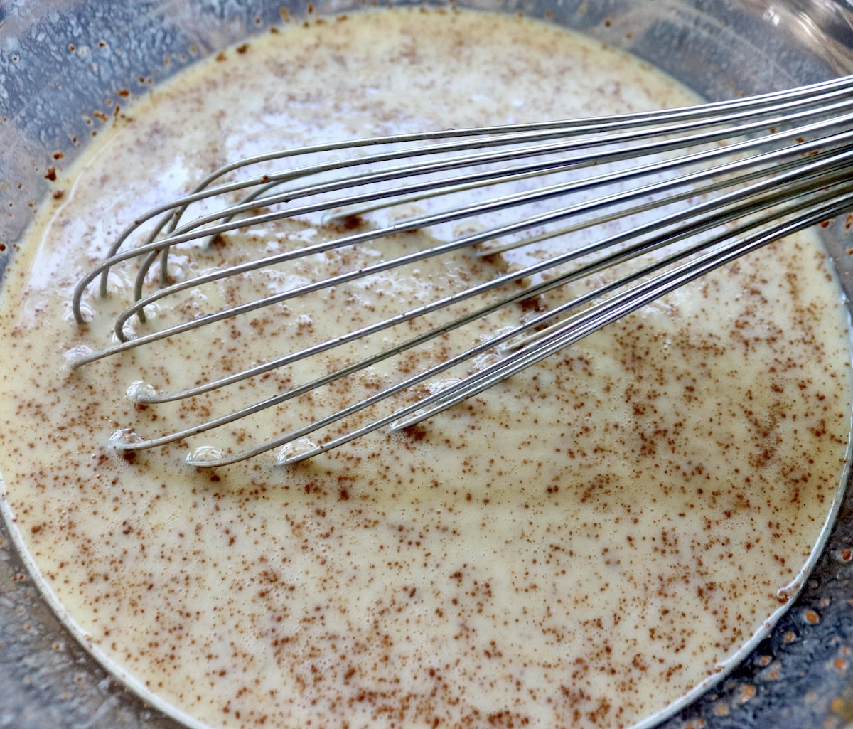Buttermilk-egg mixture for French toast in a glass bowl with a whisk.