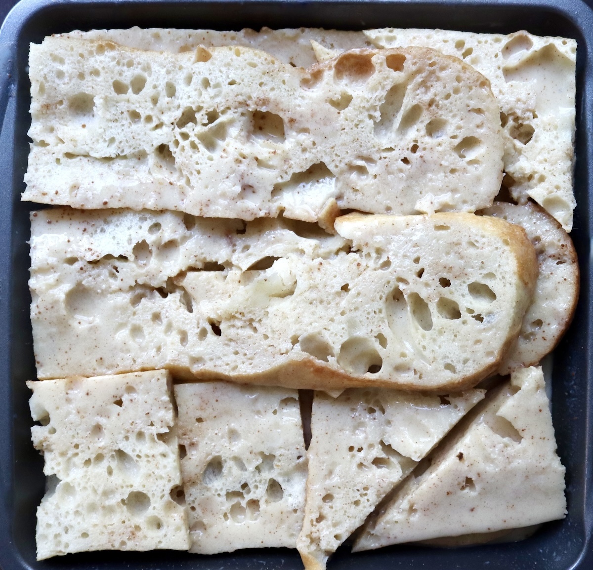 French toast bread submerged in egg-milk mixture in a square baking pan.