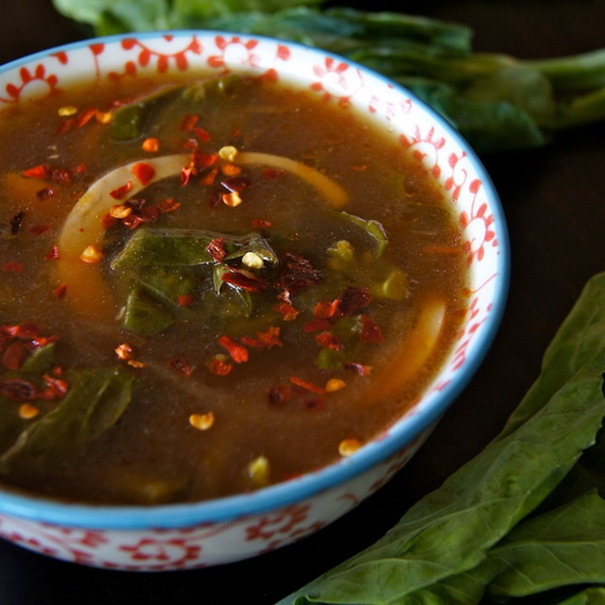 Gai-Lan-Recipe-with-Garlic-and-Coconut Miso Gai Lan Egg Soup Recipe in a white and red floral, ceramic bowl with a light blue rim, surrounded with fresh gai lan.