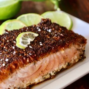 Blackened Salmon with three slime slices on a white plate.top view of blackened salmon fillet with lime slices on white plate.