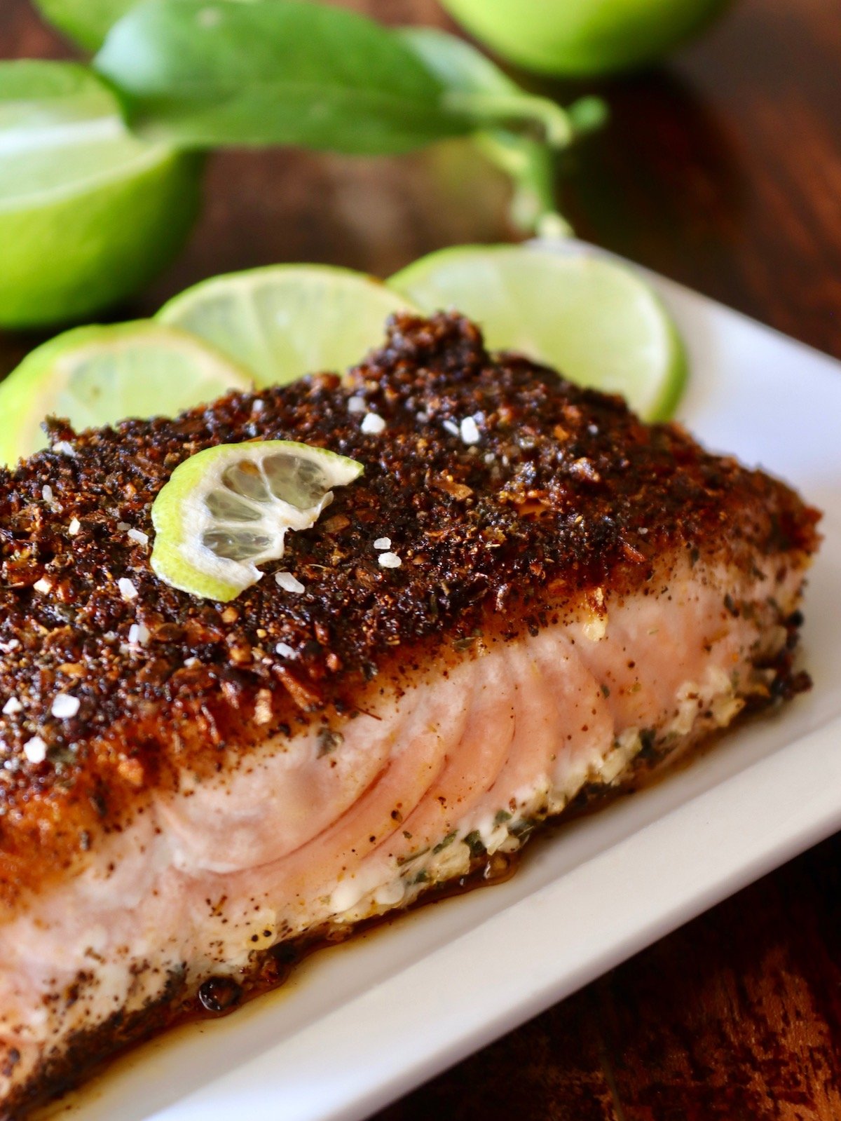 Blackened Salmon with three slime slices on a white plate.top view of blackened salmon fillet with lime slices on white plate.