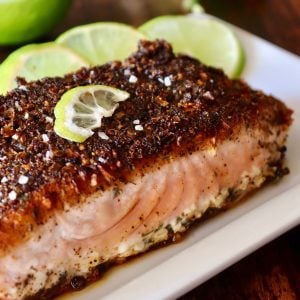 Blackened Salmon with three slime slices on a white plate.top view of blackened salmon fillet with lime slices on white plate