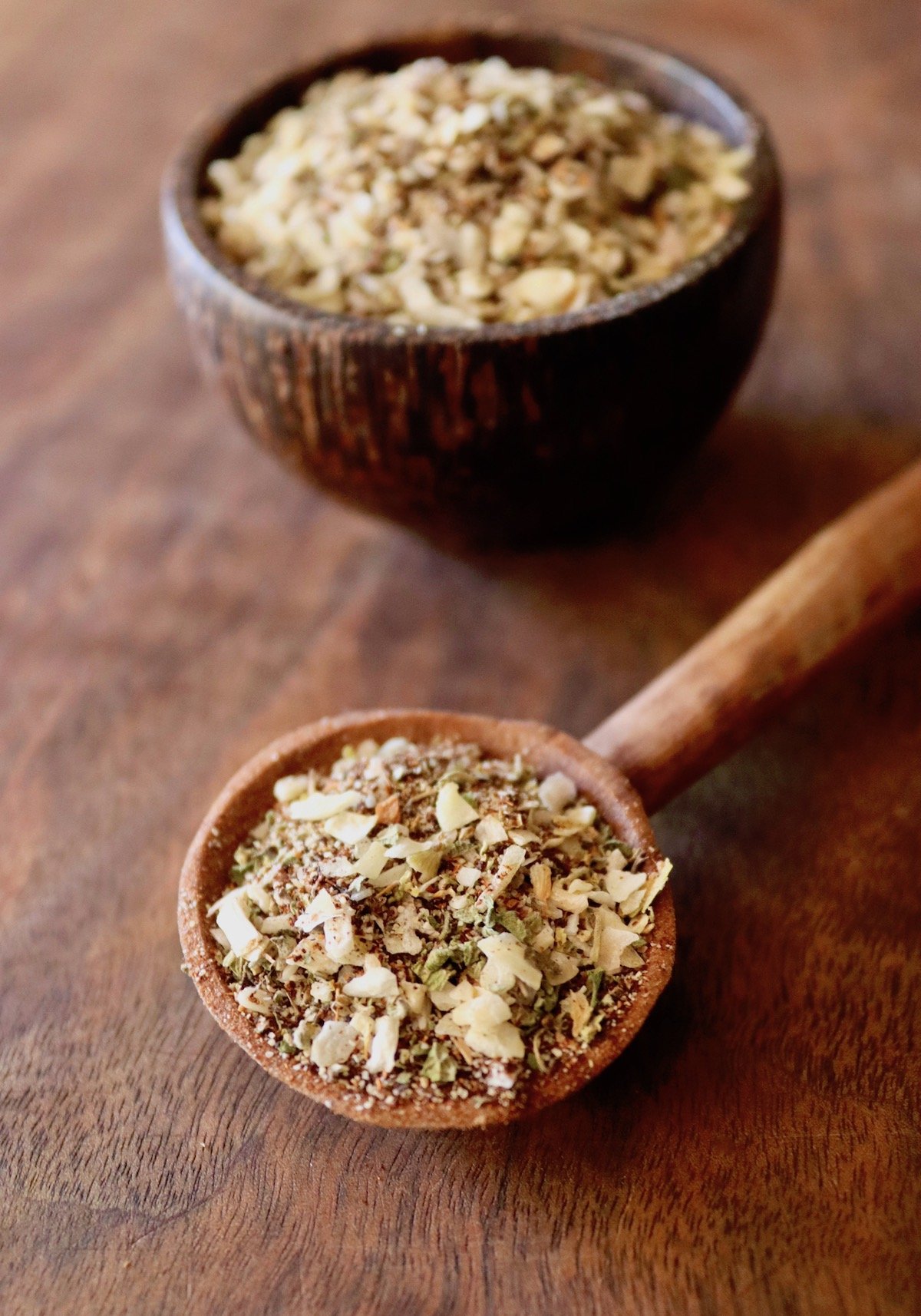 Dried spice mix of garlic, onion, chili and oregano in a wooden spoon on wood surface.