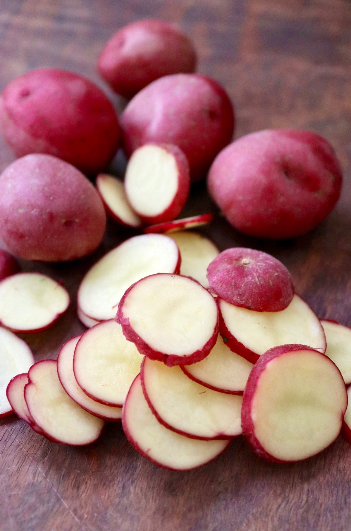 some sliced and some whole baby red potatoes on wood cutting board