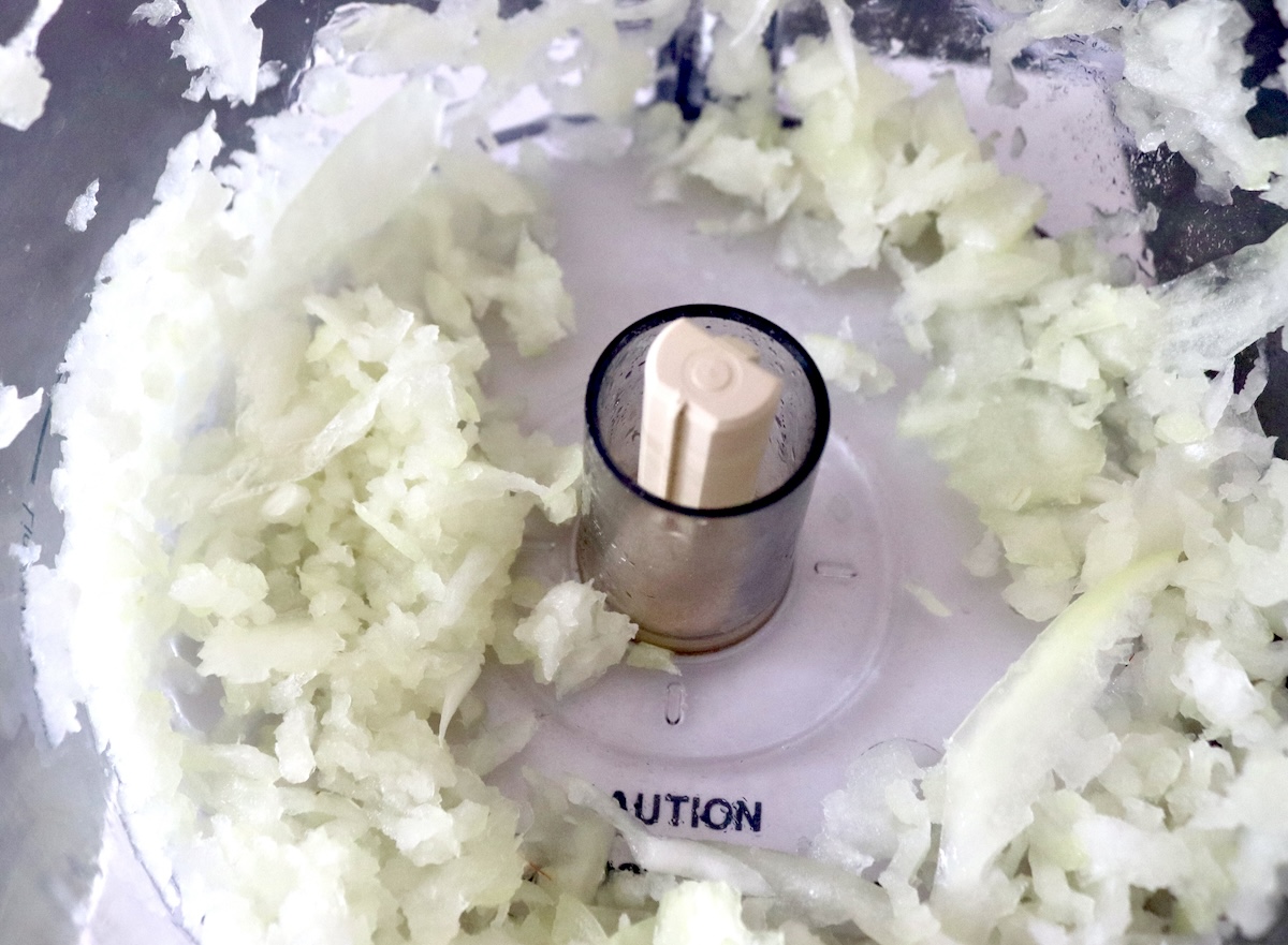 Cabbage-Potato-Pancakes Grated onion in the bowl of a food processor.