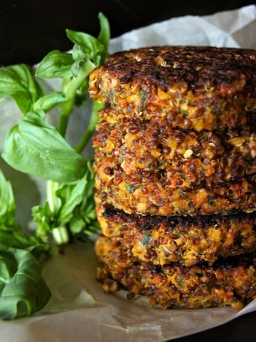 stack of 5 quinoa burgers wiht fresh basil next to it