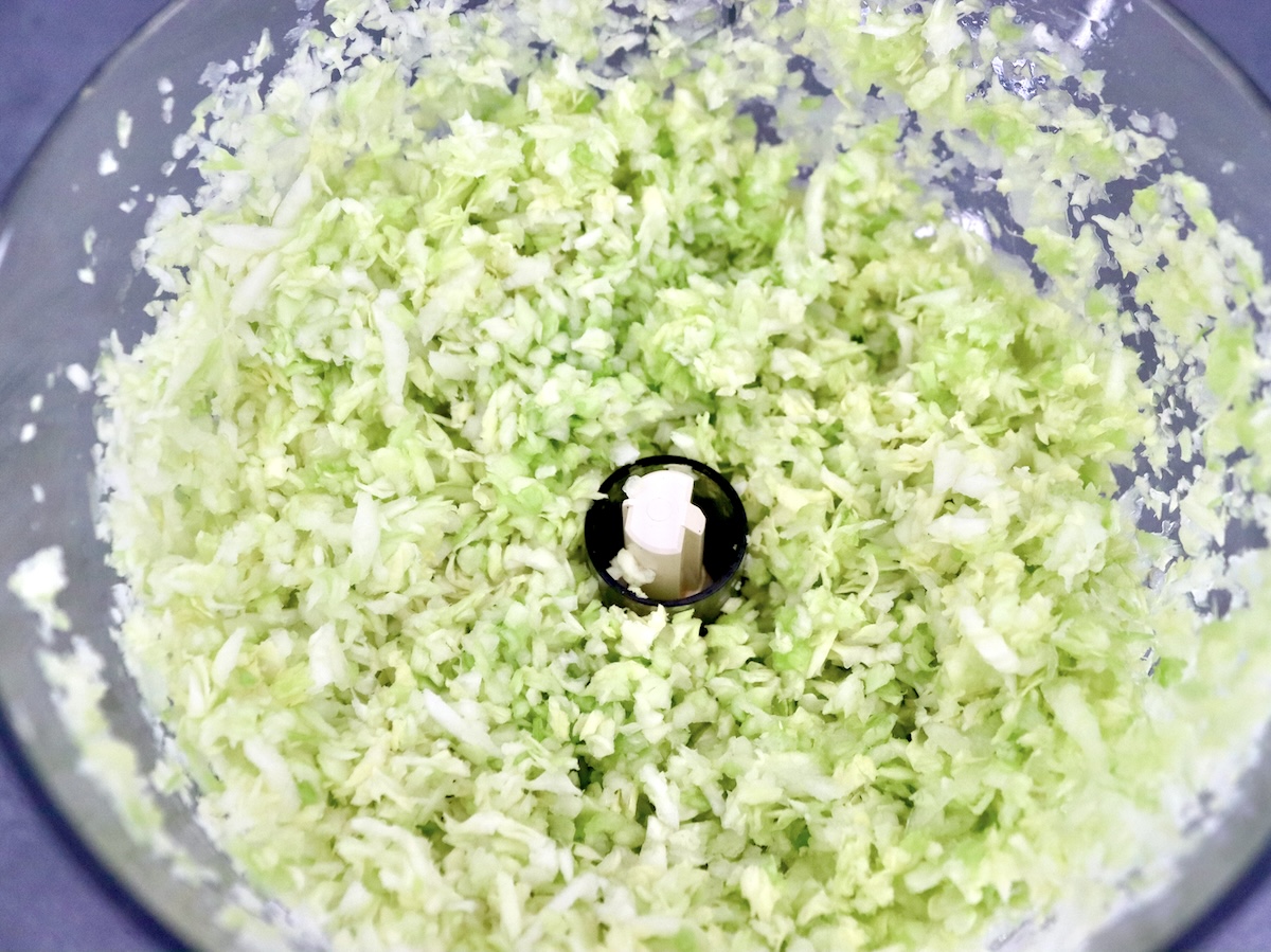 Cabbage-Potato-Pancakes Grated green cabbage in the bowl of a food processor.