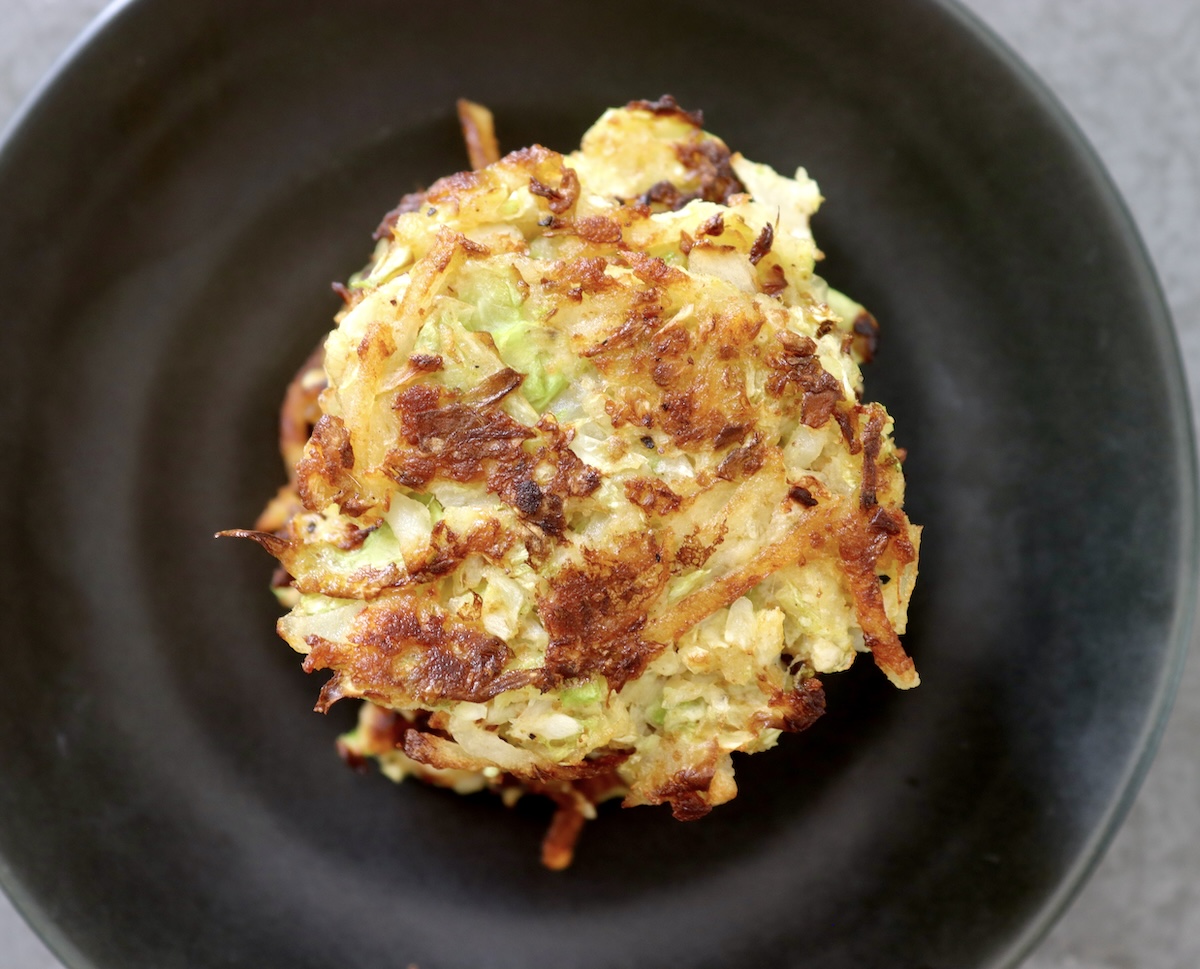 Cabbage-Potato-Pancakes Close up, top view of a crispy cabbage potato pancake, on a black plate.