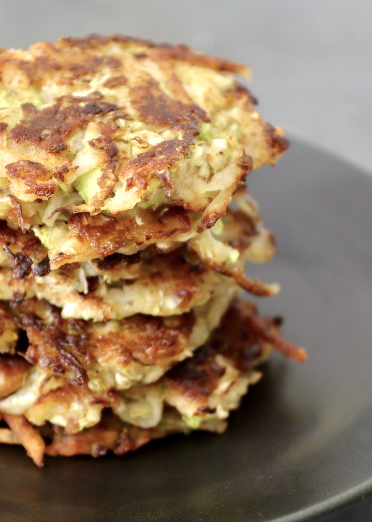 Cabbage-Potato-Pancakes Several crisped Cabbage Potato Pancakes stacked on a black plate.