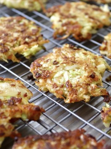 Several crisped, golden-brown cabbage potato pancakes on a wire cooling rack.