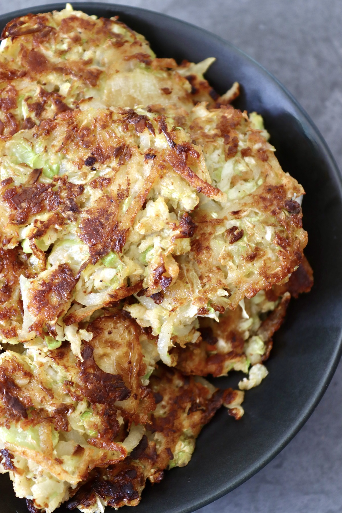Cabbage-Potato-Pancakes Several cabbage potato pancakes on a black plate.