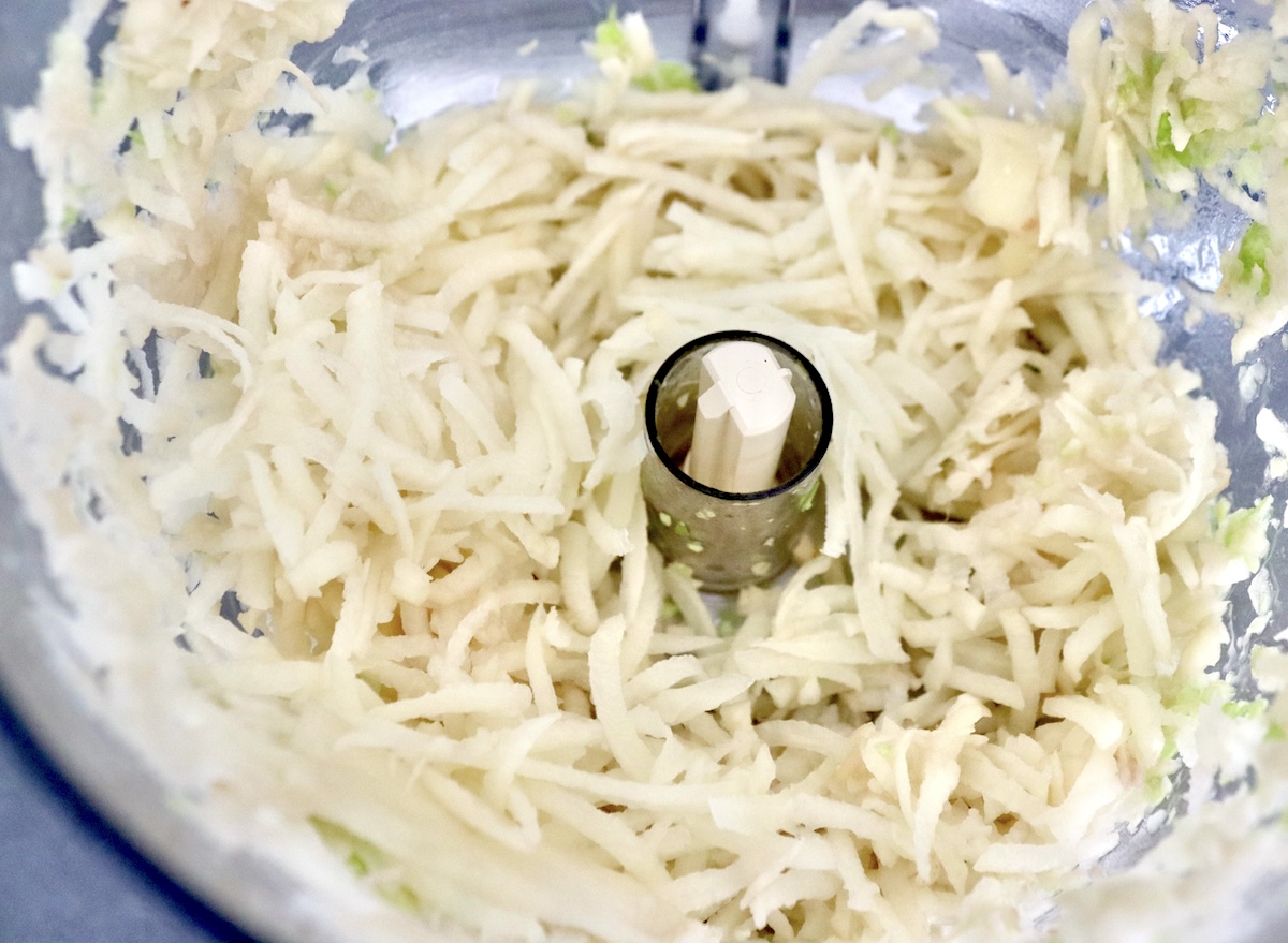 Cabbage-Potato-Pancakes Grated potatoes in the bowl of a food processor.