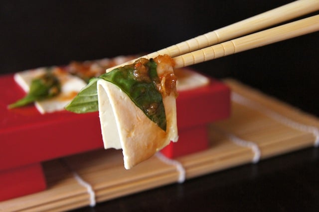 Tofu Sashimi on a red tray and one slice being held up with chopsticks.